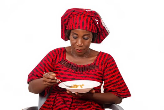 beautiful adult woman wearing red loincloth is sitting on a chair ready to eat an African meal while being smiling
