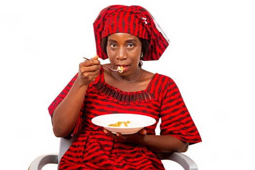 beautiful adult woman wearing red loincloth is sitting on a chair ready to eat an African meal while being smiling