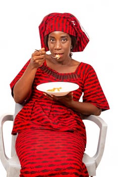 beautiful adult woman wearing red loincloth is sitting on a chair ready to eat an African meal while being smiling
