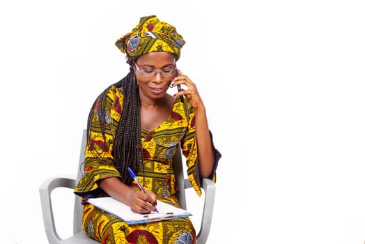 adult businesswoman sitting smiling and talking on the phone while writing in the notebook