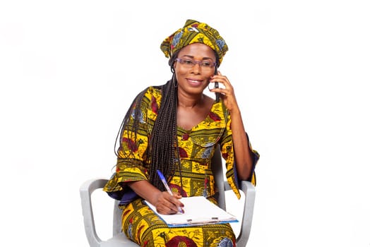 adult businesswoman sitting smiling and talking on the phone while writing in the notebook