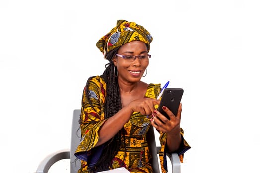 Portrait of happy adult businesswoman sitting pointing on smartphone screen outdoors writing in her notebook