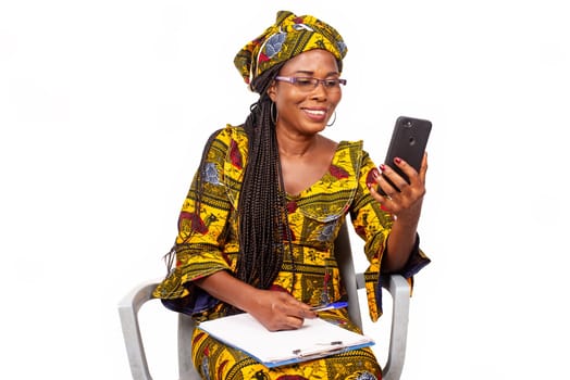 Portrait of happy adult businesswoman sitting taking selfie or making a video call with smartphone outside writing in her notebook