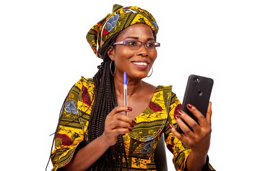 happy beautiful african mature woman sitting making a video call in her mobile telepone holding her pen in hand