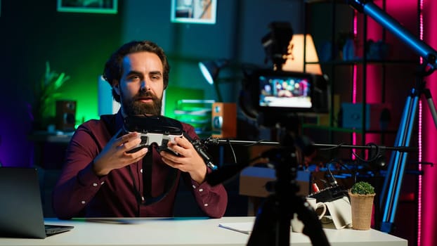 Close up shot of futuristic VR goggles held by man reviewing them for viewers. Internet star filming technology channel vlog for gadget enthusiasts, showcasing virtual reality headset, camera A