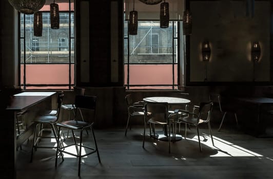 Royal Tunbridge Wells, UK - Apr 29, 2025 - Table at a restaurant with sunlight coming in through the Large windows, casting light and shadow patterns on the floor, wooden dining tables and chairs, surrounded by dark shadows inside empty room. use it as your Wallpaper, Poster and Copy space, Selective focus.