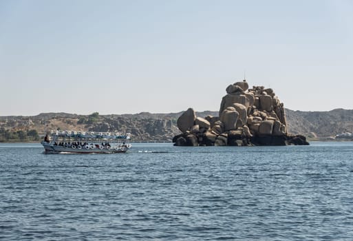 Tourists in ferry boat passing rocky island on way to Philae Temple in Aswan reservoir