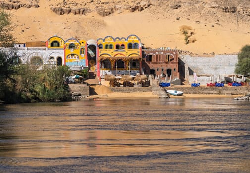 Fast flowing waters of River Nile with colorful Nubian hotels and bars near Aswan in Egypt