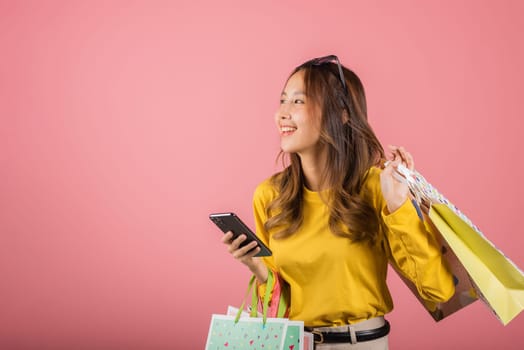 Portrait Asian happy beautiful young woman teen shopper smiling standing excited holding online shopping bags online colorful multicolor on mobile phone on hand studio shot isolated on pink background