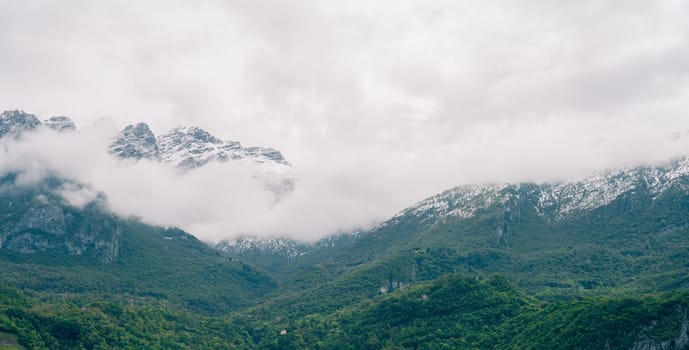 Snow-capped mountain range shrouded in mist with lush green valleys below, presenting a tranquil and scenic view