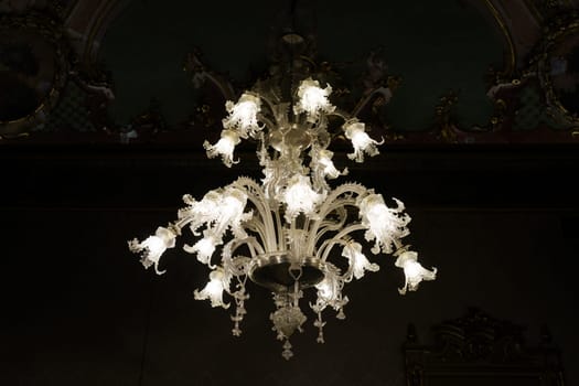 Elegant ornate glass chandelier illuminated in grand historic room with detailed ceiling decor showcasing craftsmanship and luxury