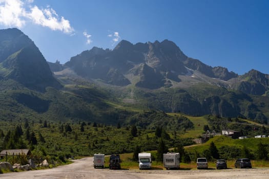 Passo Tonale, Italy - 10.08.2024: Majestic mountain landscape with blue sky and vehicles in scenic valley.