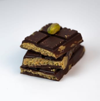 Stacked layers of kadaif embrace a generous coating of rich chocolate and are topped with a pistachio, showcasing the delightful texture and flavors in a culinary presentation.