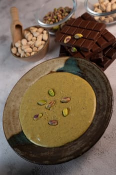 Rich pistachio cream is served in an elegant bowl, garnished with nuts, alongside chocolate pieces and additional nuts in Dubai's vibrant culinary scene.
