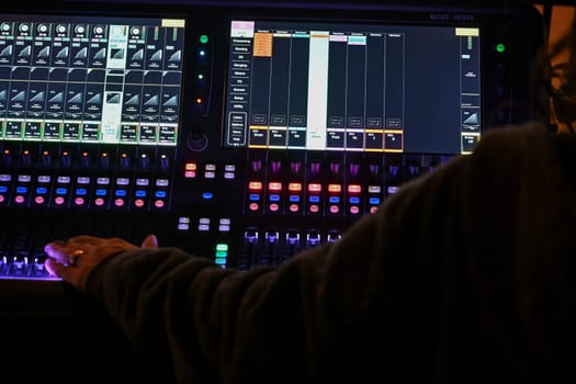 Focused sound engineer adjusts sliders and knobs on a digital mixing console while preparing for a performance in a lively venue atmosphere.