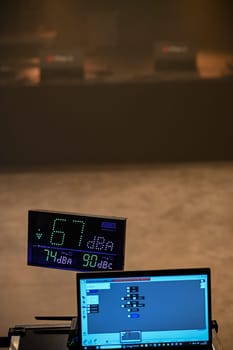 Sound level is monitored at a concert, showing 67 dBA on a digital display. A laptop runs software for tracking decibel levels as part of audio management.