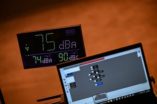 Sound level is monitored at a concert, showing 73 dBA on a digital display. A laptop runs software for tracking decibel levels as part of audio management.