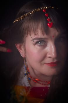 A mature blonde woman poses elegantly in a striking sari, adorned with cultural jewelry and striking makeup, capturing a lively atmosphere.