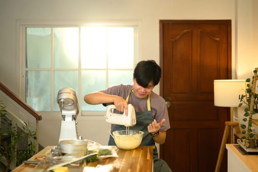 Young asian man using a hand mixer to whip ingredients for compound butter.
