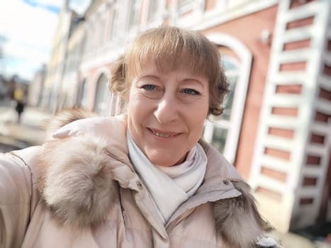 A middle aged female blogger enjoys a sunny day outdoors, capturing her cheerful selfie while exploring the city streets.