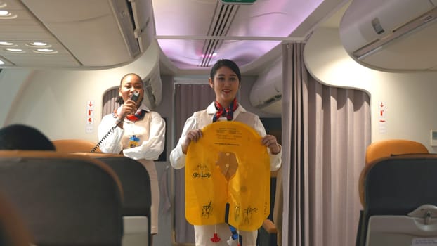 Asian stewardess safety explaining passengers prior to flight take off in airplane, air hostess uniform safety demonstration presenting pre-flight safety instructions life vest in emergency situation