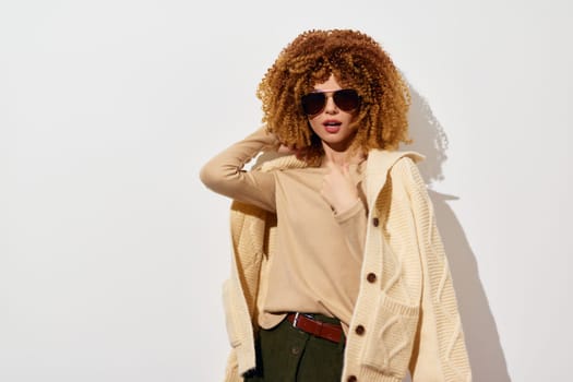 Fashionable woman in an oversized cardigan and sunglasses poses confidently against a minimalist white background, representing modern style and chic elegance