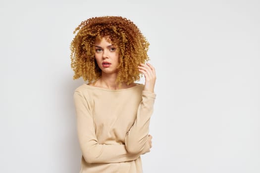 A woman with beautiful curly hair poses against a plain white background, wearing a beige top Her confident stance and soft expression highlight the beauty of natural curls, creating an uplifting vi