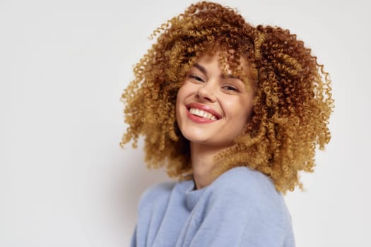A vibrant young woman with voluminous curly hair radiates happiness as she smiles brightly The neutral background enhances her joyful expression, making it ideal for beauty and lifestyle imagery