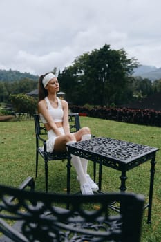 A young woman dressed in a sporty outfit sits gracefully outdoors, reflecting a serene vibe in a green landscape, perfect for themes of wellness and outdoor activities