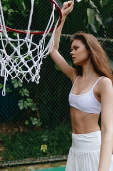 Confident young woman in white sports attire, engaged in basketball outdoors, highlighting fitness, athleticism, and a vibrant green background, encouraging an active lifestyle