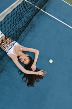 A young woman, dressed in a white sporty outfit, lies gracefully on a blue tennis court, exuding calmness and relaxation, complemented by a tennis ball and vibrant colors