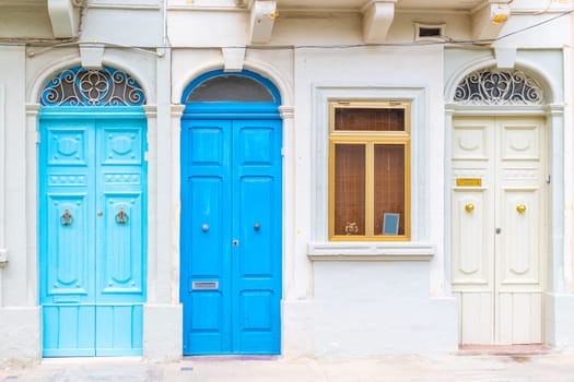 Facade of a residential building with three locked wooden doors painted in light blue, blue and white color.