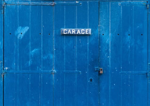 Blue wooden garage door with the inscription - Garage. Closed garage gate with a small lock on it.