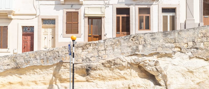 Wide image showing multiple entrance doors and windows of a residential building in Malta.