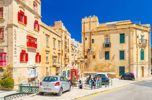 Valletta, Malta - April 2, 2025: A street view of Valletta with traditional architecture, parked cars, London red phone booth and a group of tourists