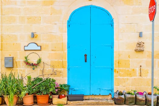 Residential building facade made of stone brick with metal door painted blue, potted plants near it and a stop traffic road sign