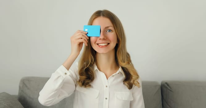 Portrait of happy smiling young woman holding plastic credit bank card, joyful girl customer of a modern bank sitting on the couch in living room at home