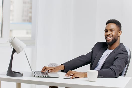 Focused businessman typing on laptop while surrounded by paperwork and a steaming coffee cup in a modern office.