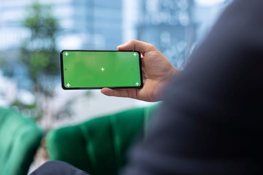 Focused chief executive officer looks at chroma key display on phone, examining infographics data in his office. Young business administrator implementing investment strategy.