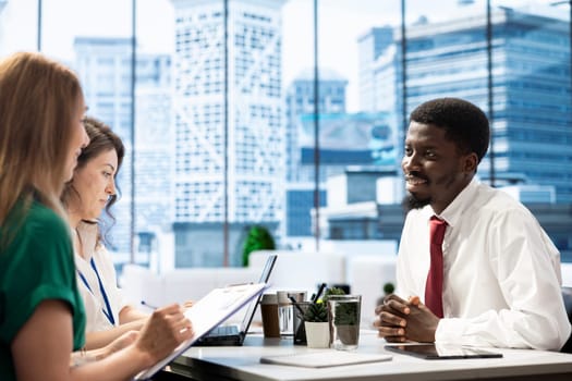 Human resources team looking at african american man CV, sitting at office desk. HR department staff members selecting candidates to work for company, reading person resume