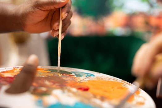 African american painter mixing watercolor paints on a palette before applying on canvas, using painting technique to create beautiful masterpiece for fine art gallery. Artistic workshop. Close up.