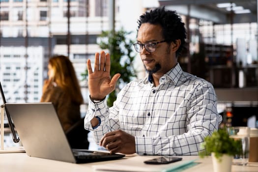 Black man employee joins a telecommuting session at his office desk, multitasking between project management and business strategy discussions. Productivity and collaboration across departments.