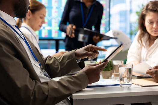 Shareholder examining infographics and resource allocation on tablet, gathering with associates for a strategy session. Utilizing data analytics to develop innovative solutions for growth.