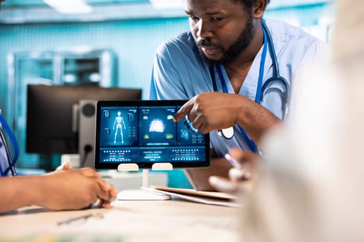 Healthcare medical staff discussing patient health records during a meeting, utilizing modern diagnostic tools and technology in a well equipped doctor office. Assistants work with medic.