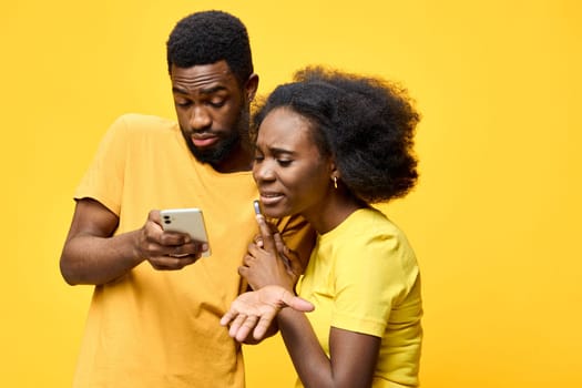 A couple in yellow attire displays emotions of frustration and concern as they check a smartphone against a vivid yellow backdrop, highlighting modern communication challenges