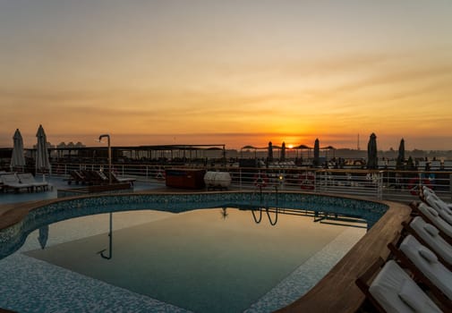 Sun rises over the swimming pool on deck of Nile cruise boat docked alongside another ship in Edfu Egypt