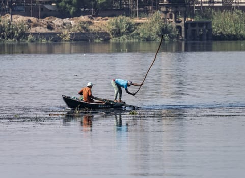 Two men in their small boat on a calm river Nile while tending to fishing net in the water