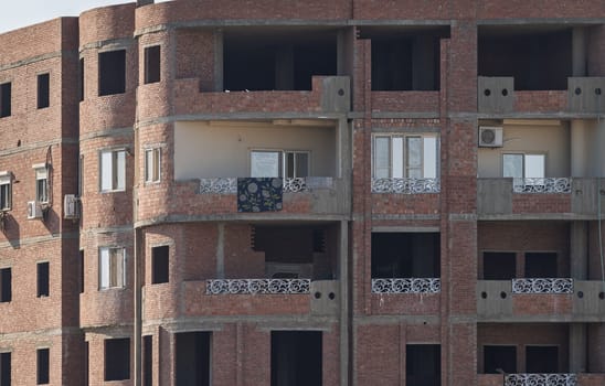 An unfinished building in Esna, Egypt, with brick and concrete construction and rebar on roof. Some apartments occupied