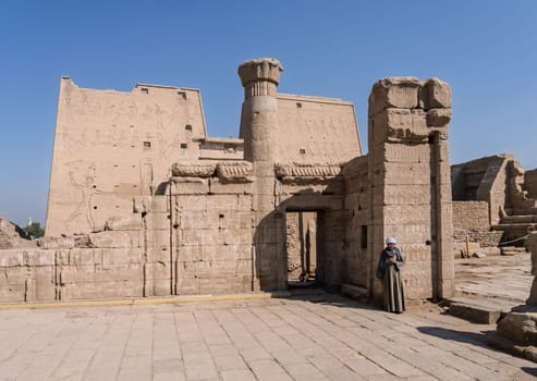 Edfu, Egypt - 6 November 2024: Single local Egyptian standing at the entrance to the massive temple in Edfu dedicated to Horus and Hathor