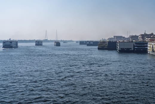 Crowded harbor in Edfu with Nile cruise boats docked and others leaving for Aswan on river in Egypt